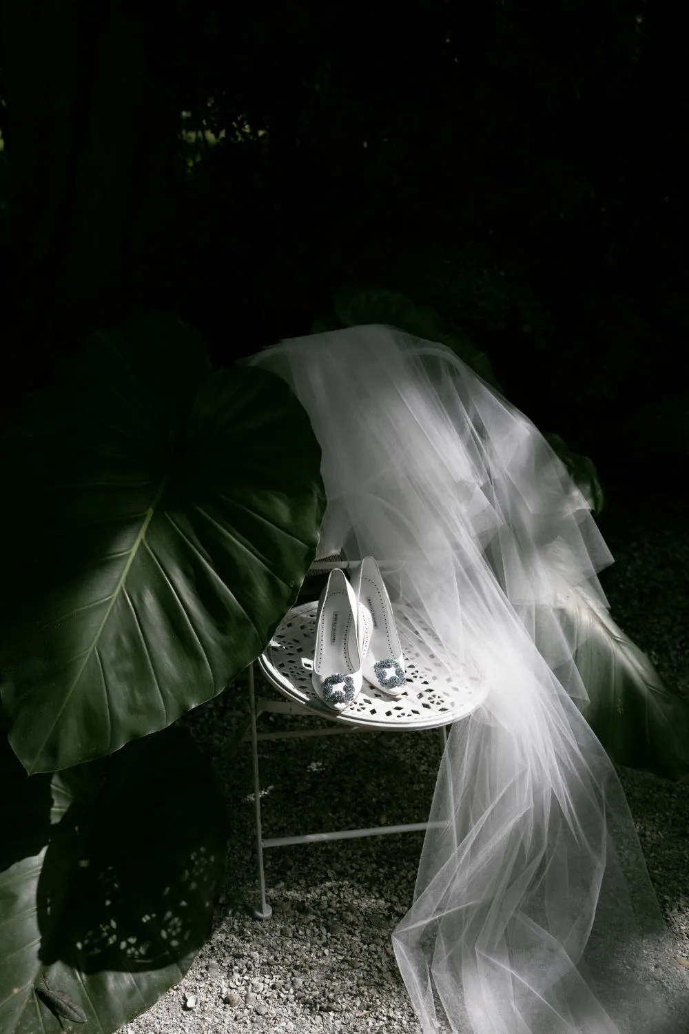 Bridal heels and a tulle veil draped over a garden chair among tropical leaves