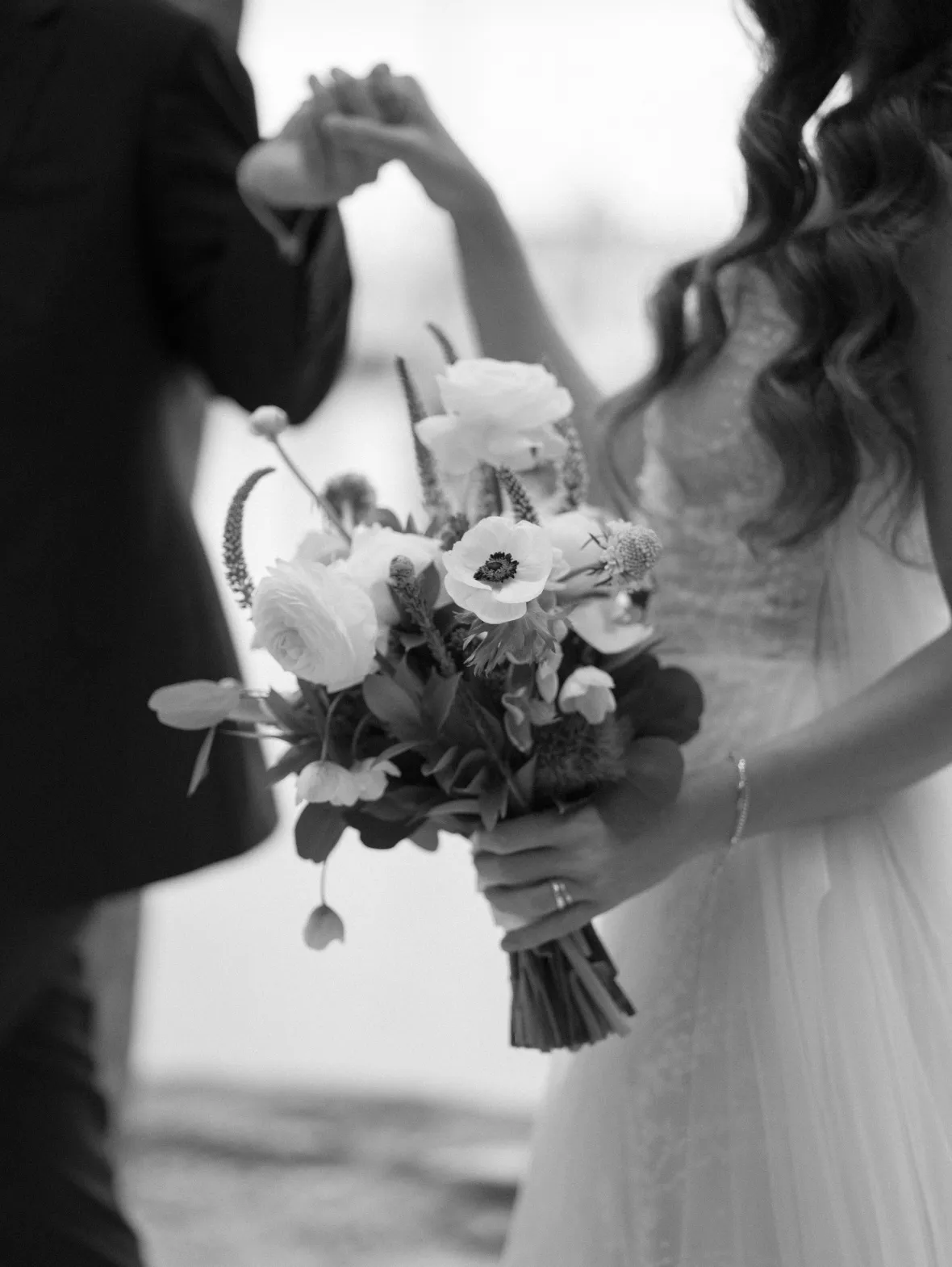 Bride holding a bouquet of anemones and ranunculus while facing the groom