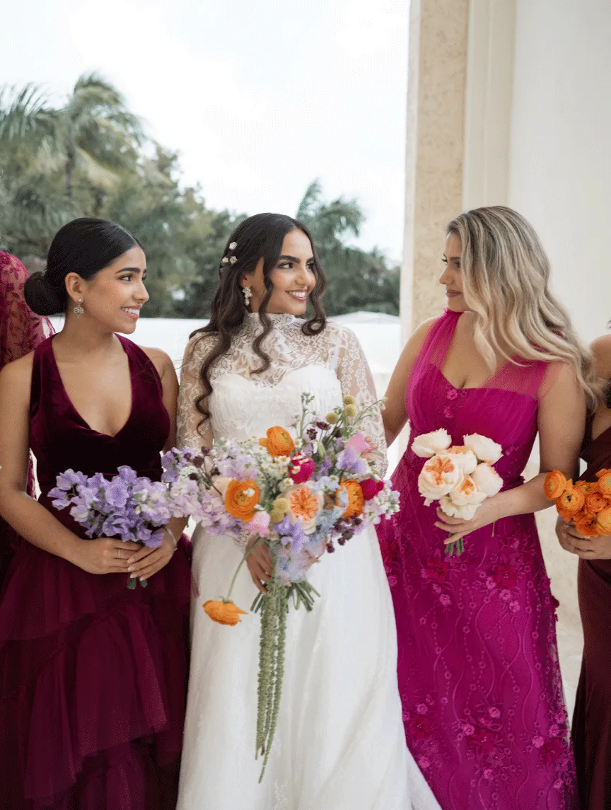 Bride in lace with bridesmaids in berry and magenta gowns holding wildflower bouquets