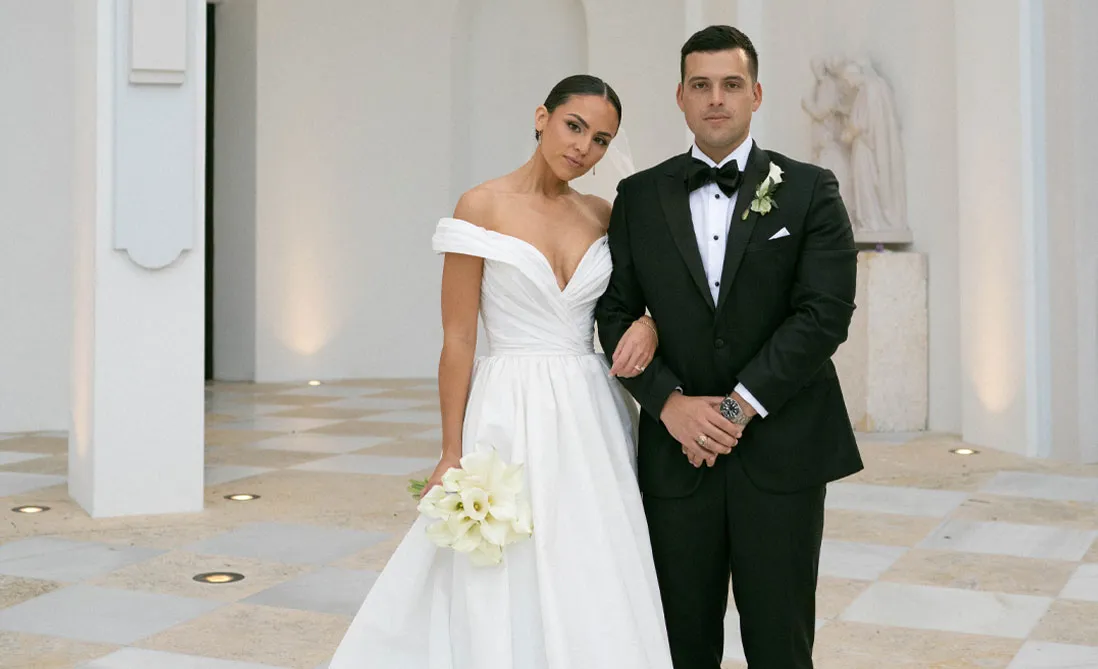 Bride with calla lily bouquet and groom in a black tuxedo in a white marble hall