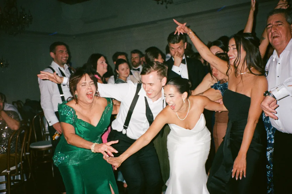 Bride and guests laughing and dancing in a crowded reception hall