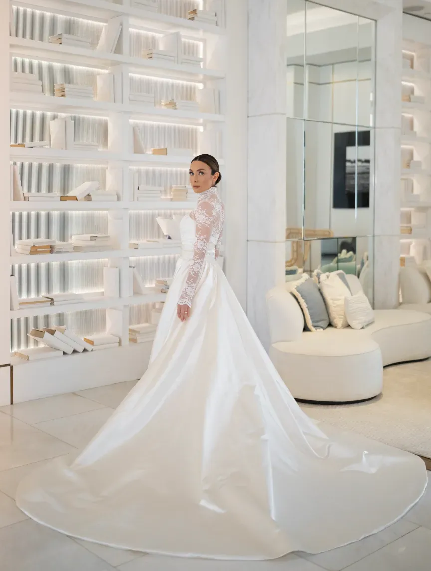 Bride in a long-sleeved lace gown with a wide satin train, glancing back