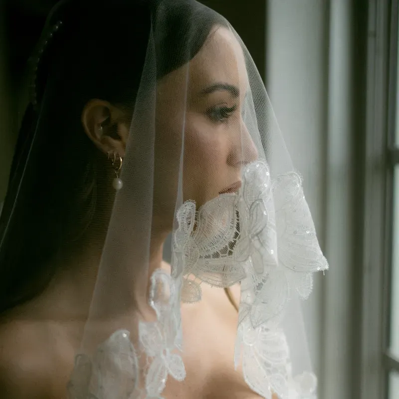Bride in profile under a lace-edged veil by a window