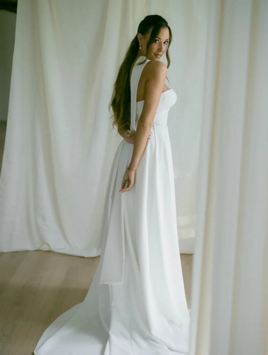 Bride in a satin halter gown glancing over her shoulder against draped curtains