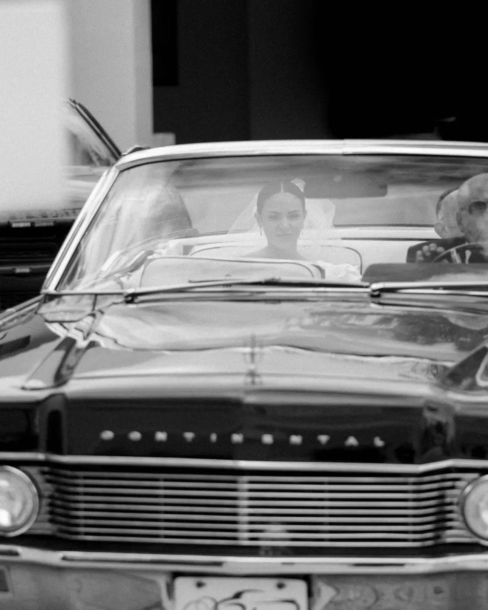 Bride in a veil riding in a vintage Lincoln Continental convertible