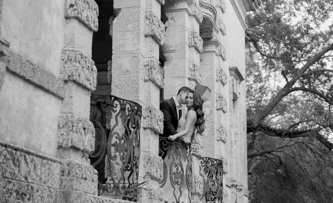 Couple embracing on a carved stone balcony behind an ornate wrought iron railing