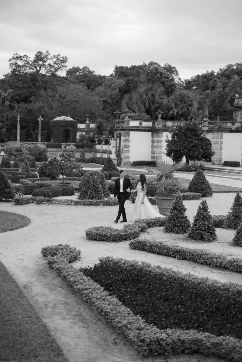 Bride and groom holding hands as they walk through a formal hedge garden