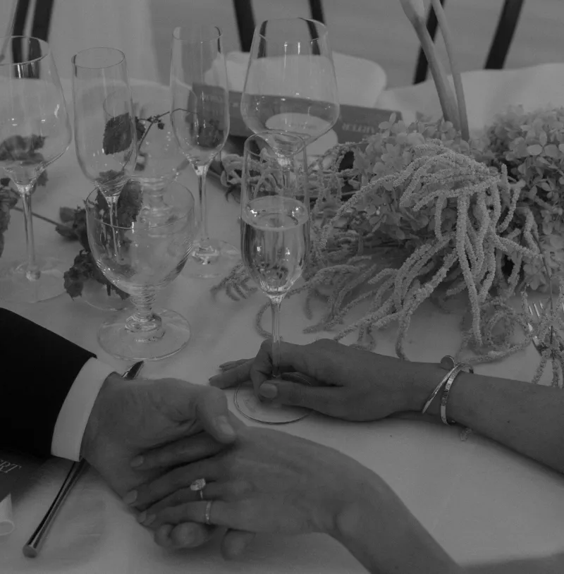 Couple holding hands at a reception table set with wine glasses and flowers