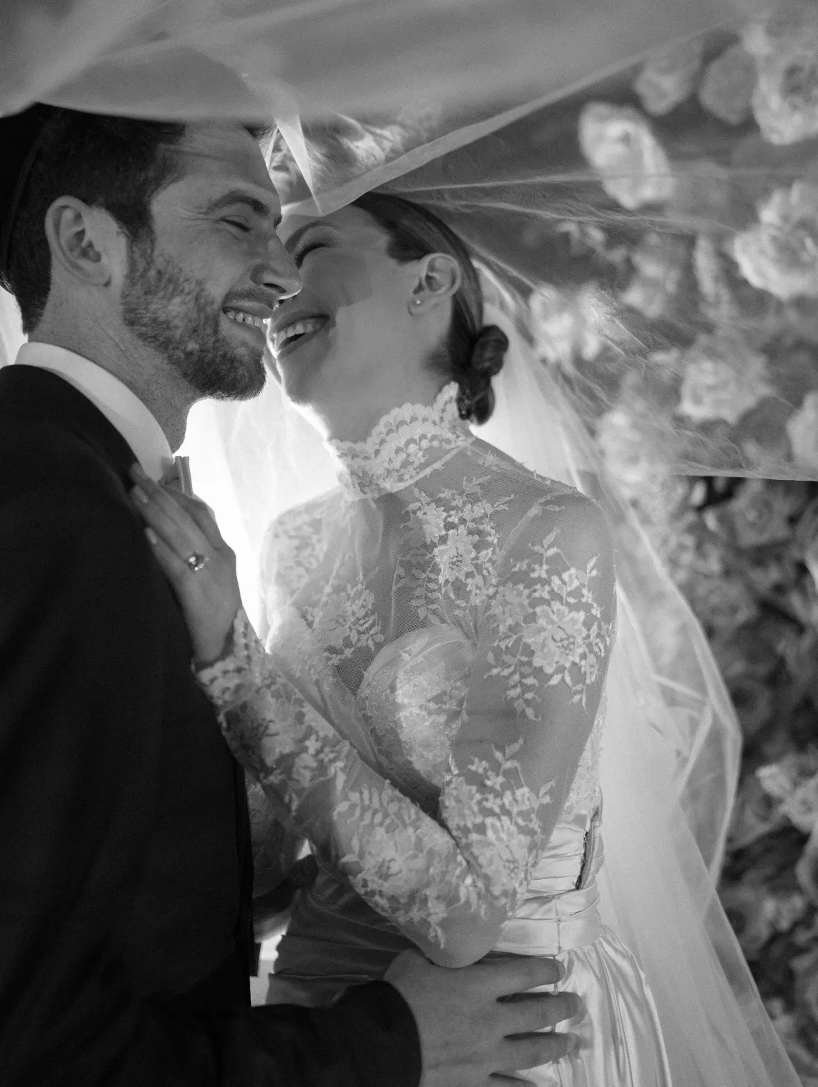 Bride in a lace high-neck gown and groom laughing together under her veil