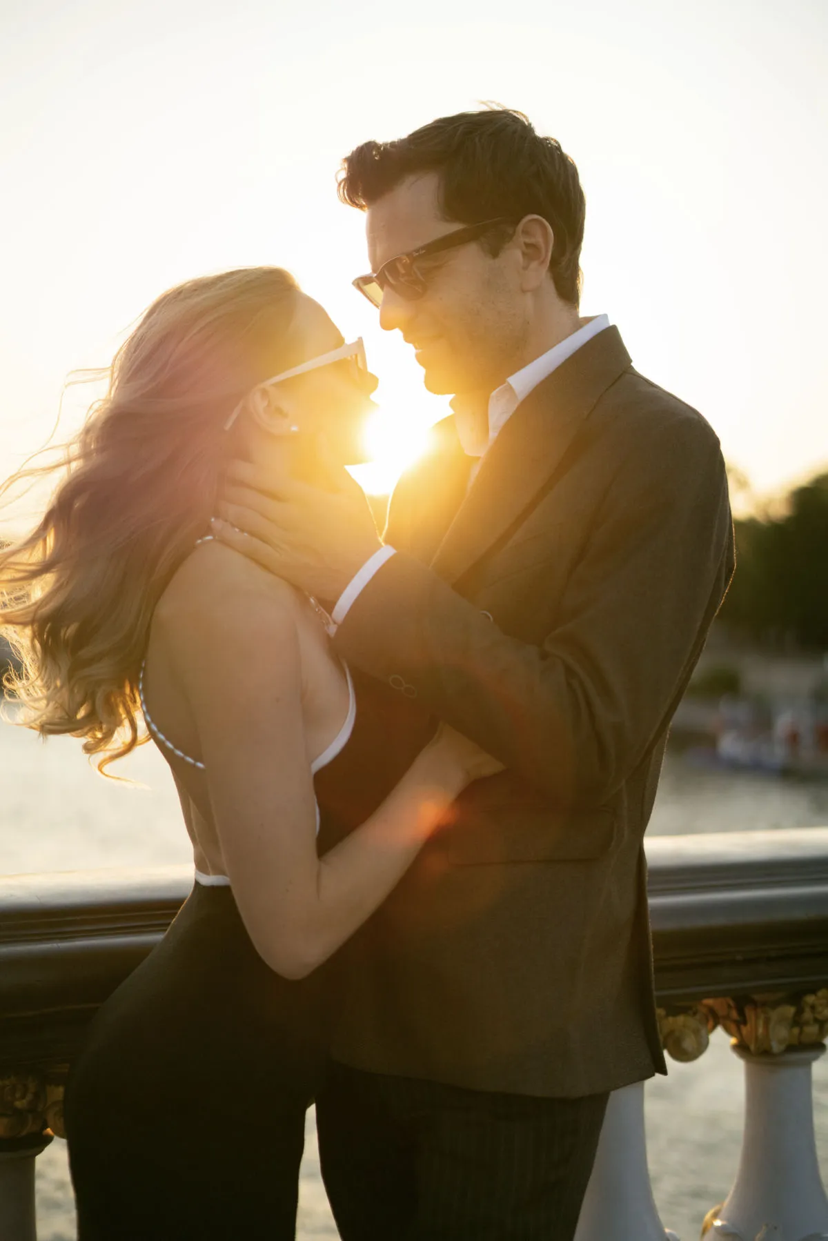 Couple in sunglasses embracing against an ornate bridge railing at sunset