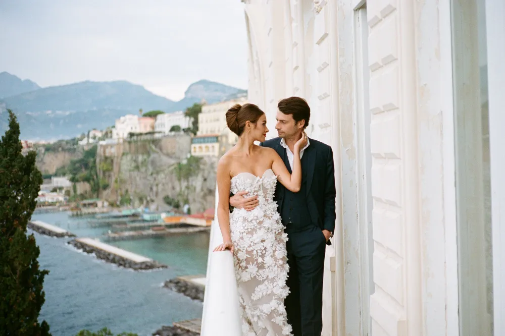 Bride and groom on a terrace above a cliffside coastal town, looking at each other