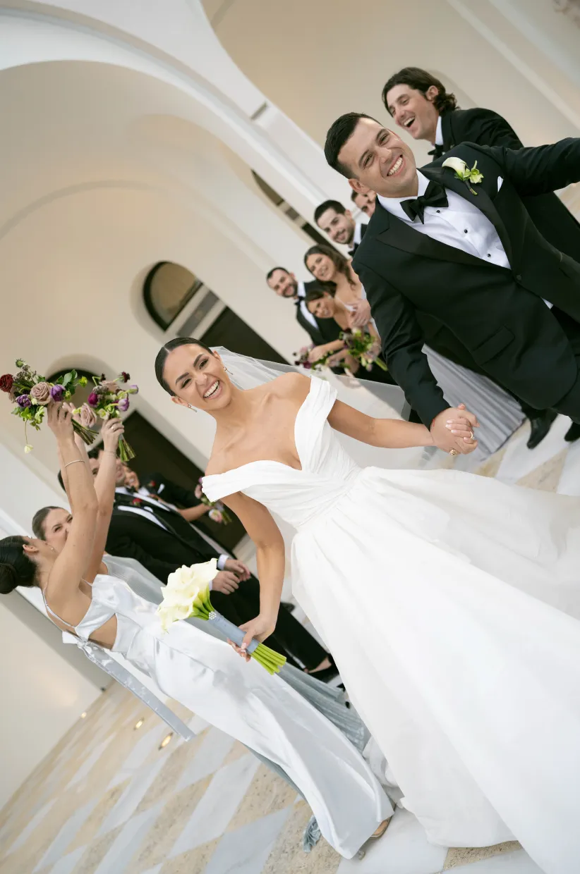 Bride and groom laughing as the wedding party cheers with bouquets raised