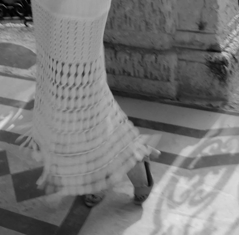 Close crop of a crocheted dress hem and heeled sandals on a patterned tile floor
