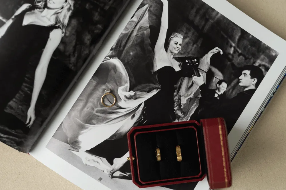 Engagement ring and two gold wedding bands in a red box, resting on an open photo book
