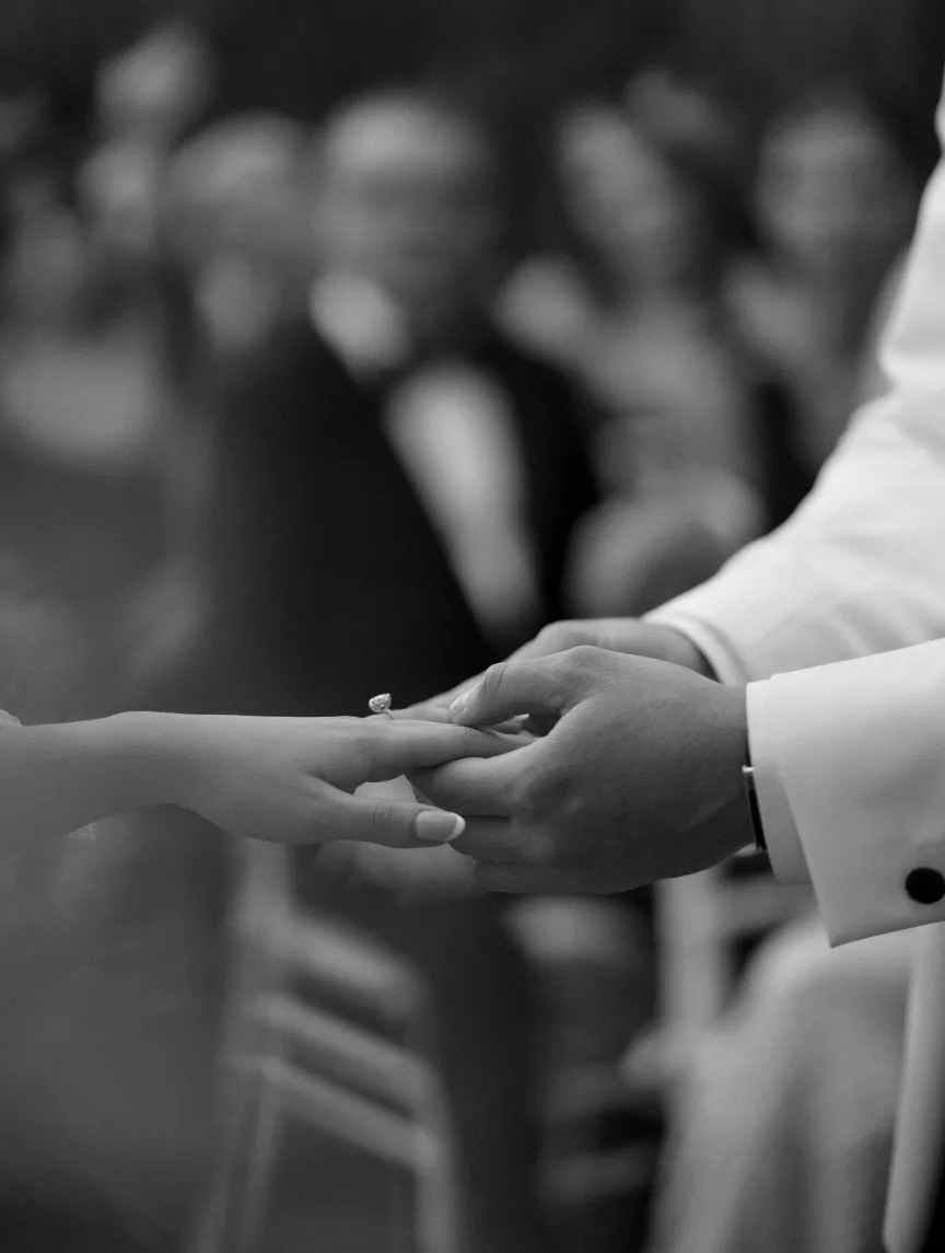 Close view of a groom holding the bride's hand during the ceremony, guests blurred behind