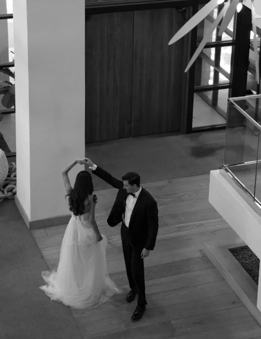 Groom twirling the bride on a wooden floor, seen from a balcony above