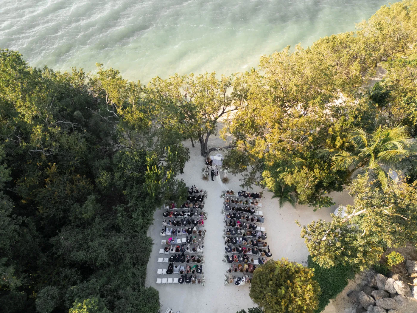 Aerial view of a beachside ceremony with guests seated under trees