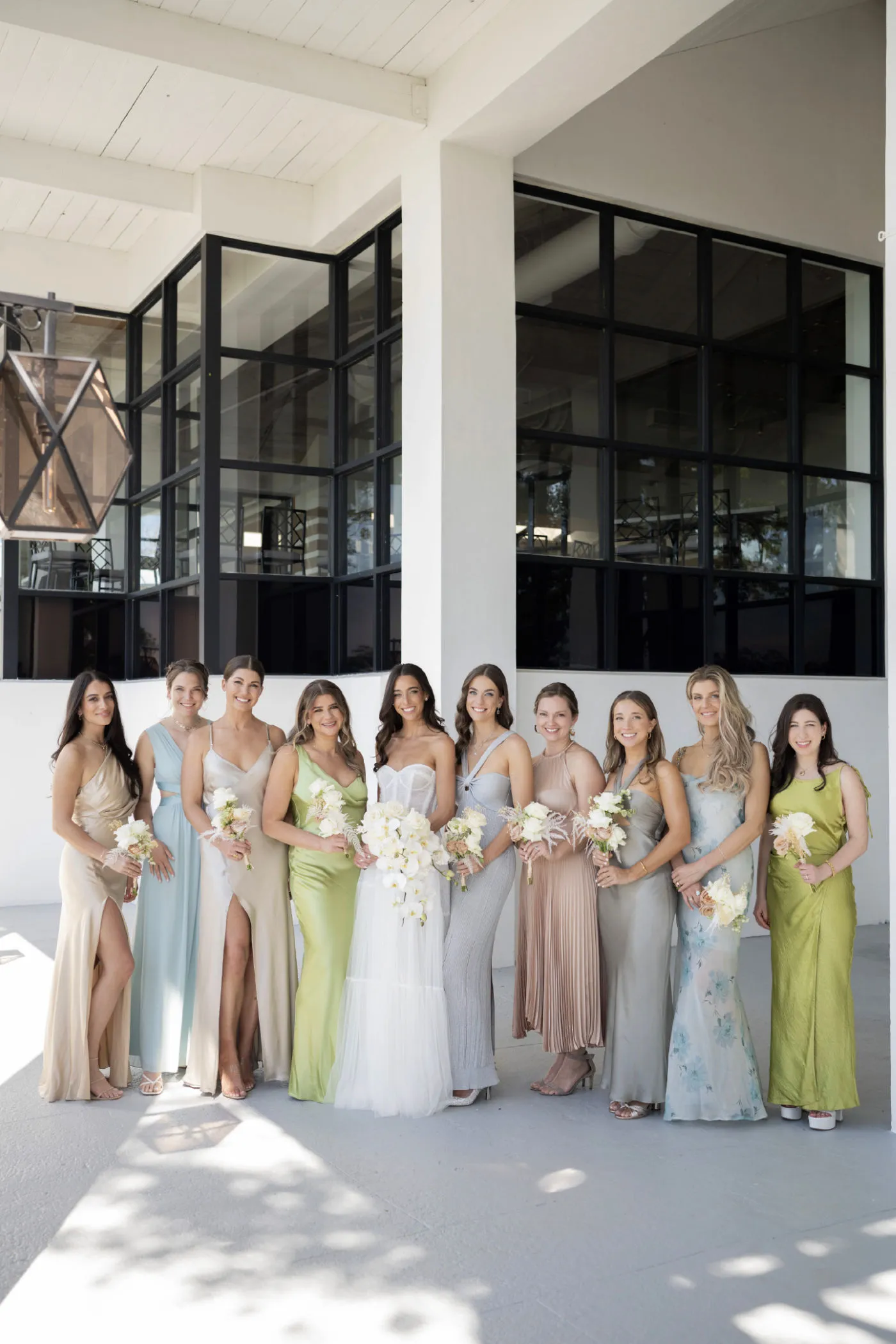 Bride with ten bridesmaids in pastel gowns holding white bouquets