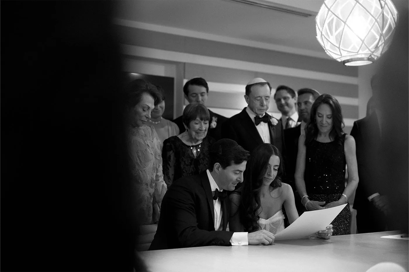 Bride and groom signing their marriage contract as family gathers behind them