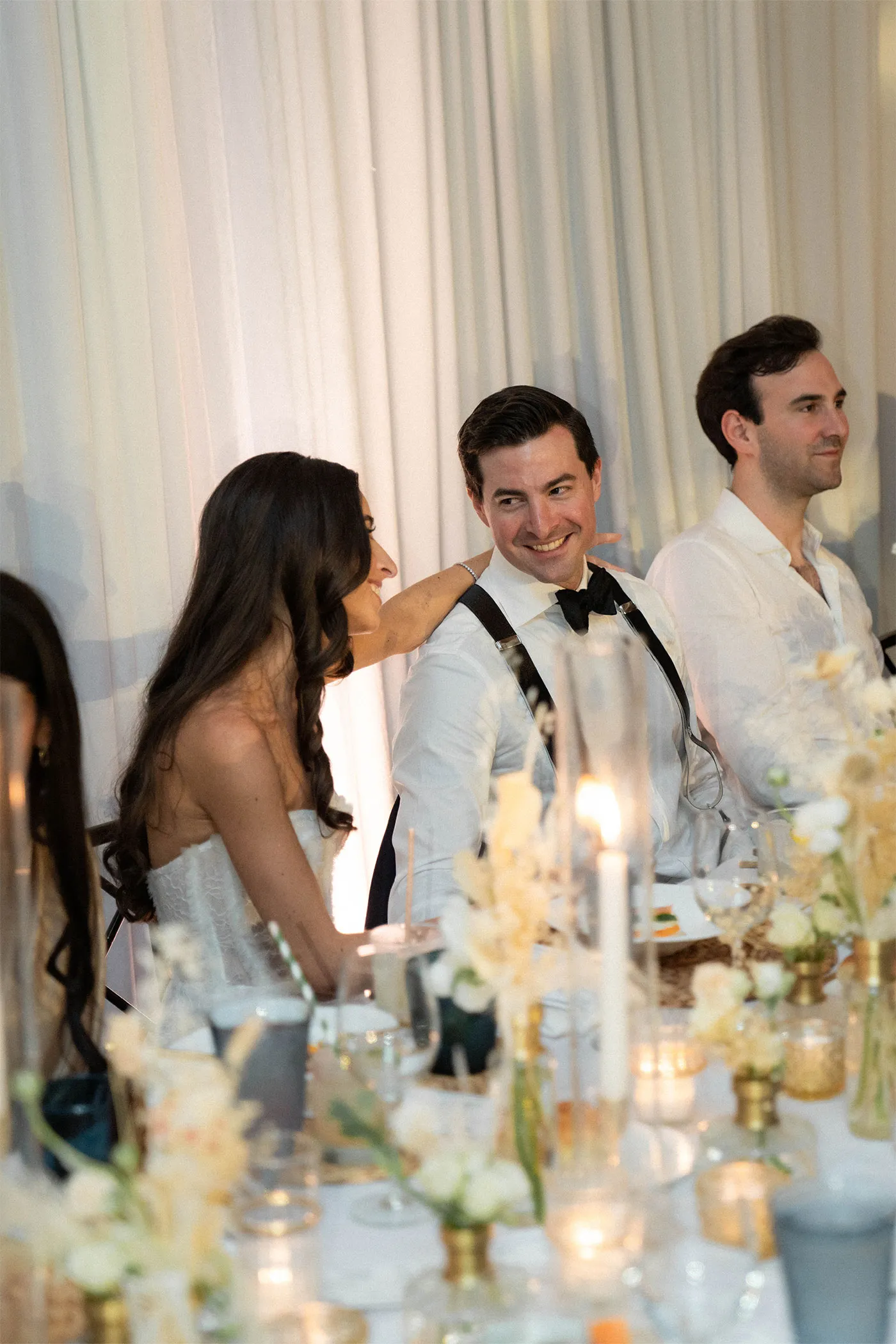 Bride resting a hand on the groom's shoulder at a candlelit reception table