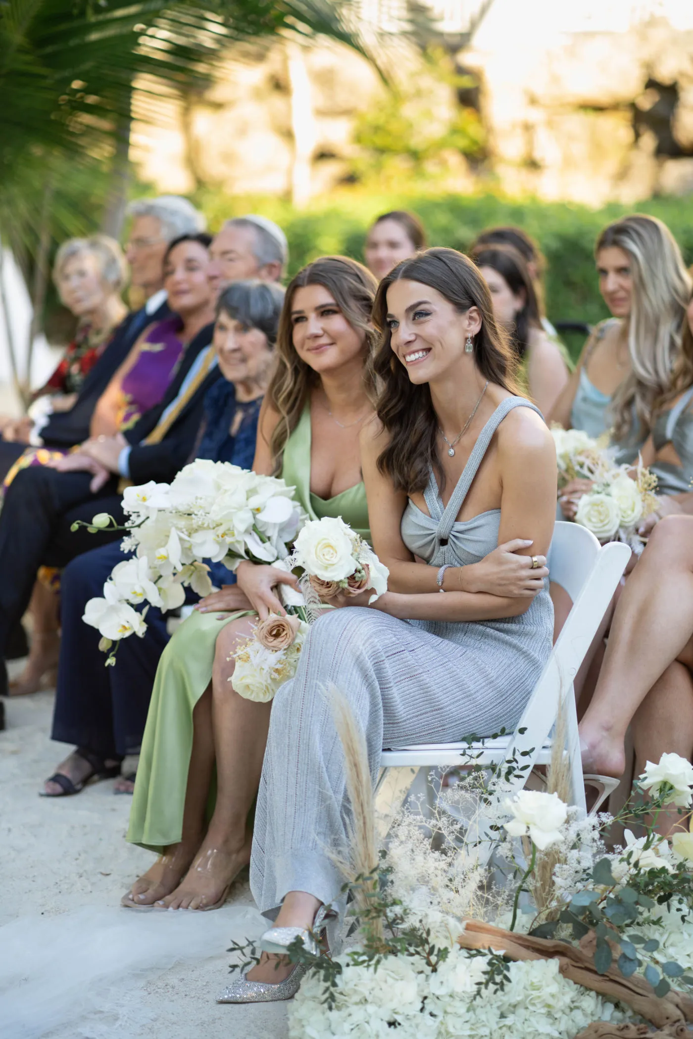 Bridesmaids holding white orchid bouquets and smiling from the front row of the ceremony
