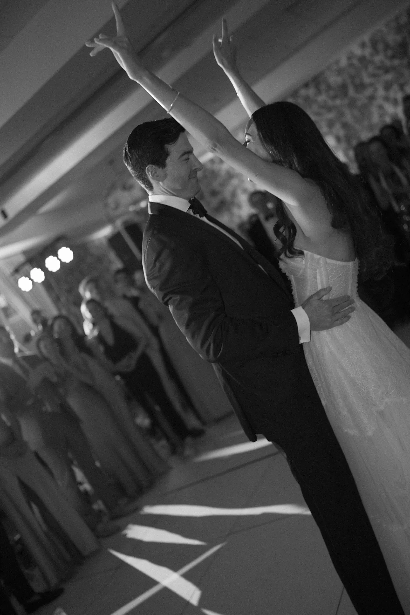 Bride and groom with arms raised on the dance floor as guests watch