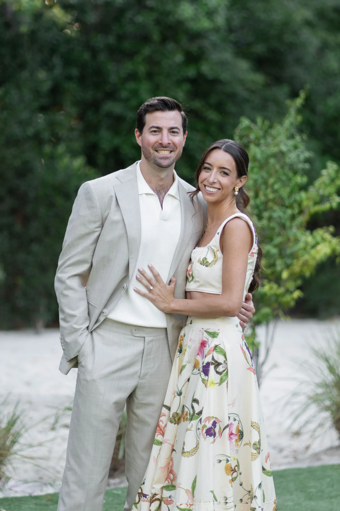 Couple in a cream suit and floral dress standing arm in arm on a lawn