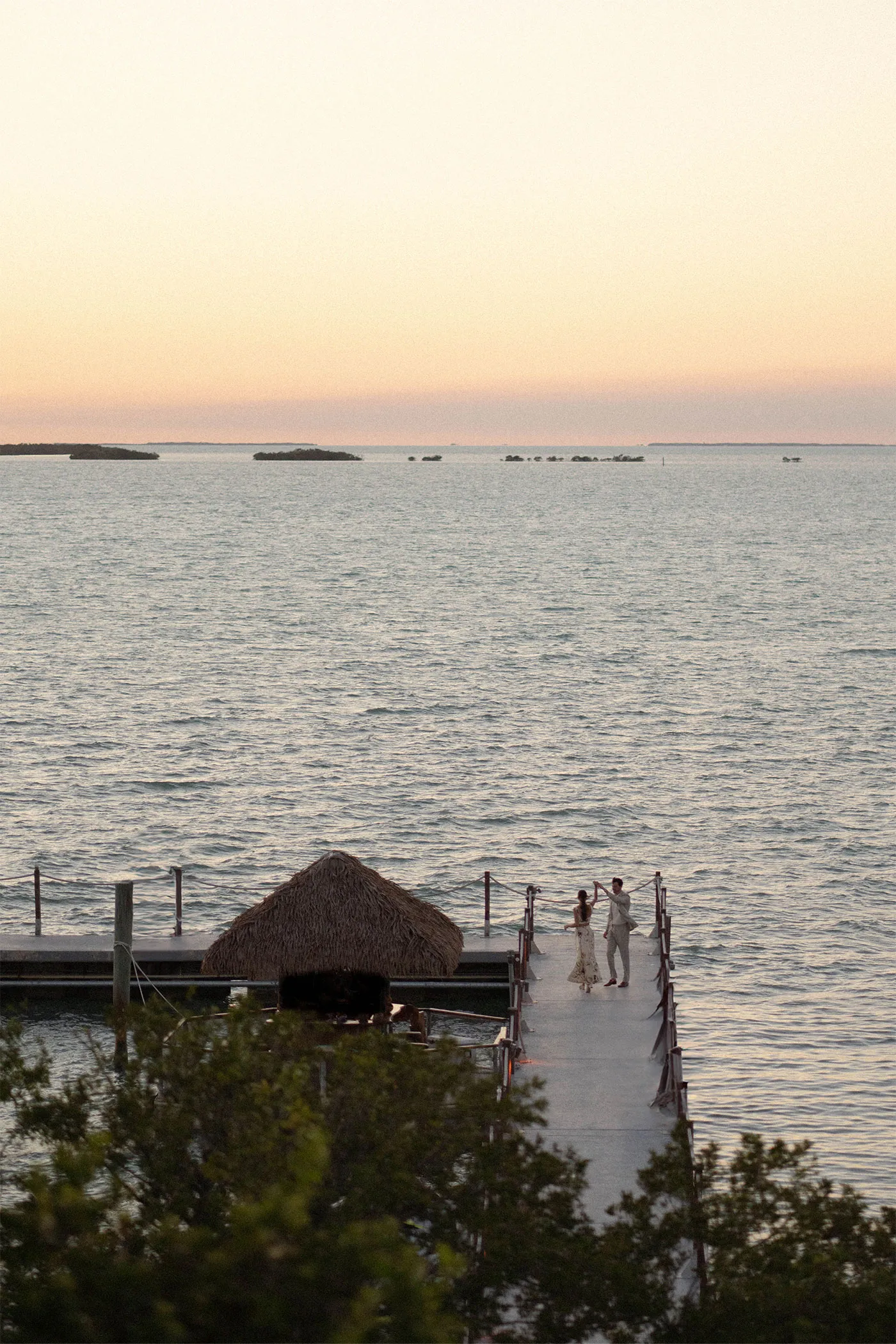 Couple dancing at the end of a long dock over calm water at dusk