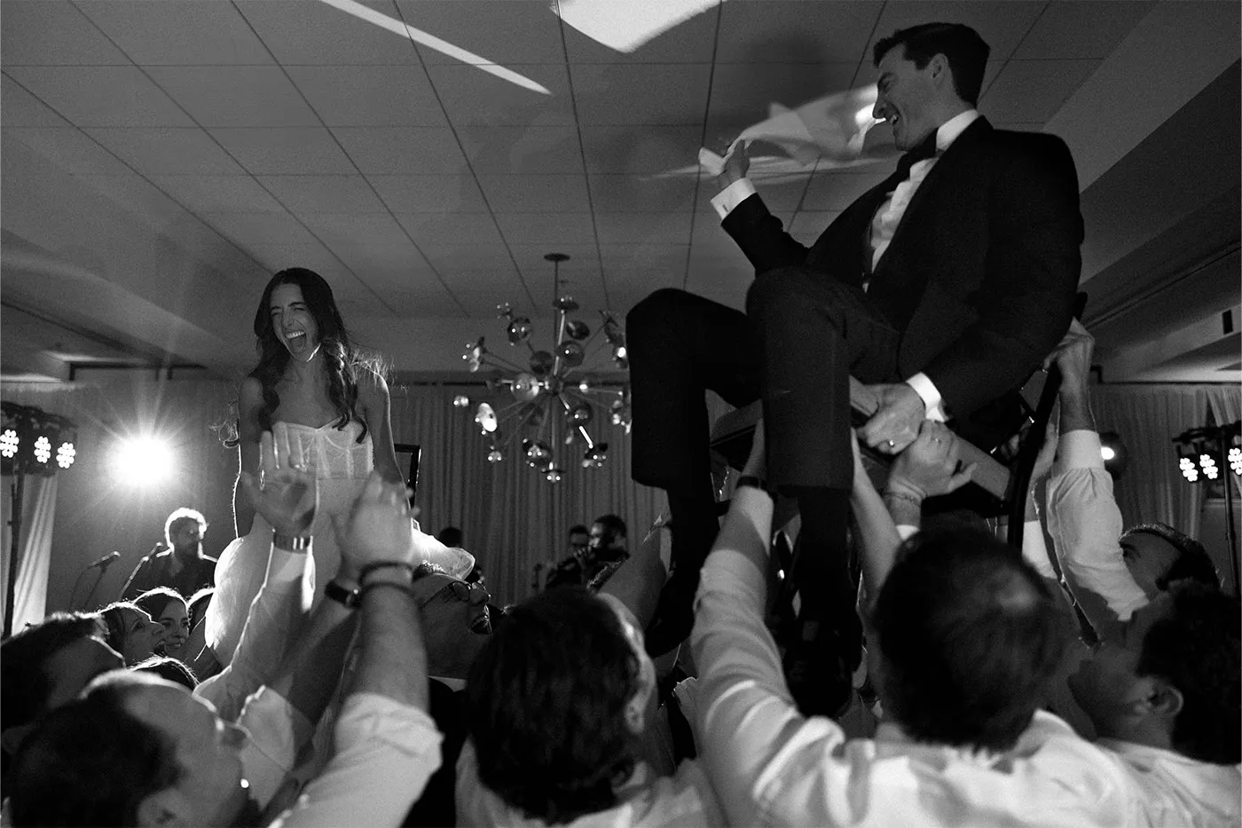 Bride and groom lifted on chairs by cheering guests during the hora