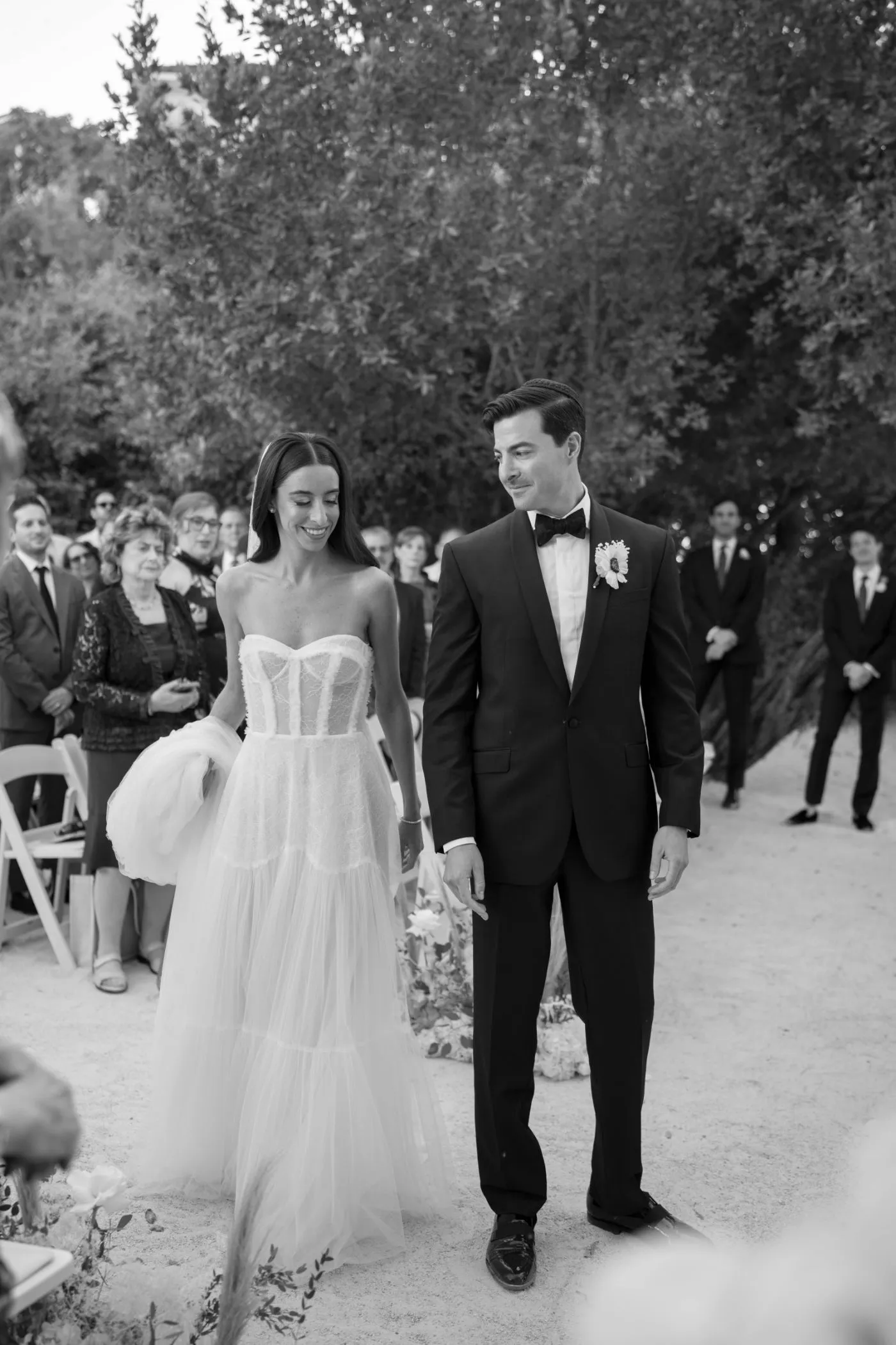 Bride in a tulle gown and groom in a tuxedo walking back up the aisle past standing guests