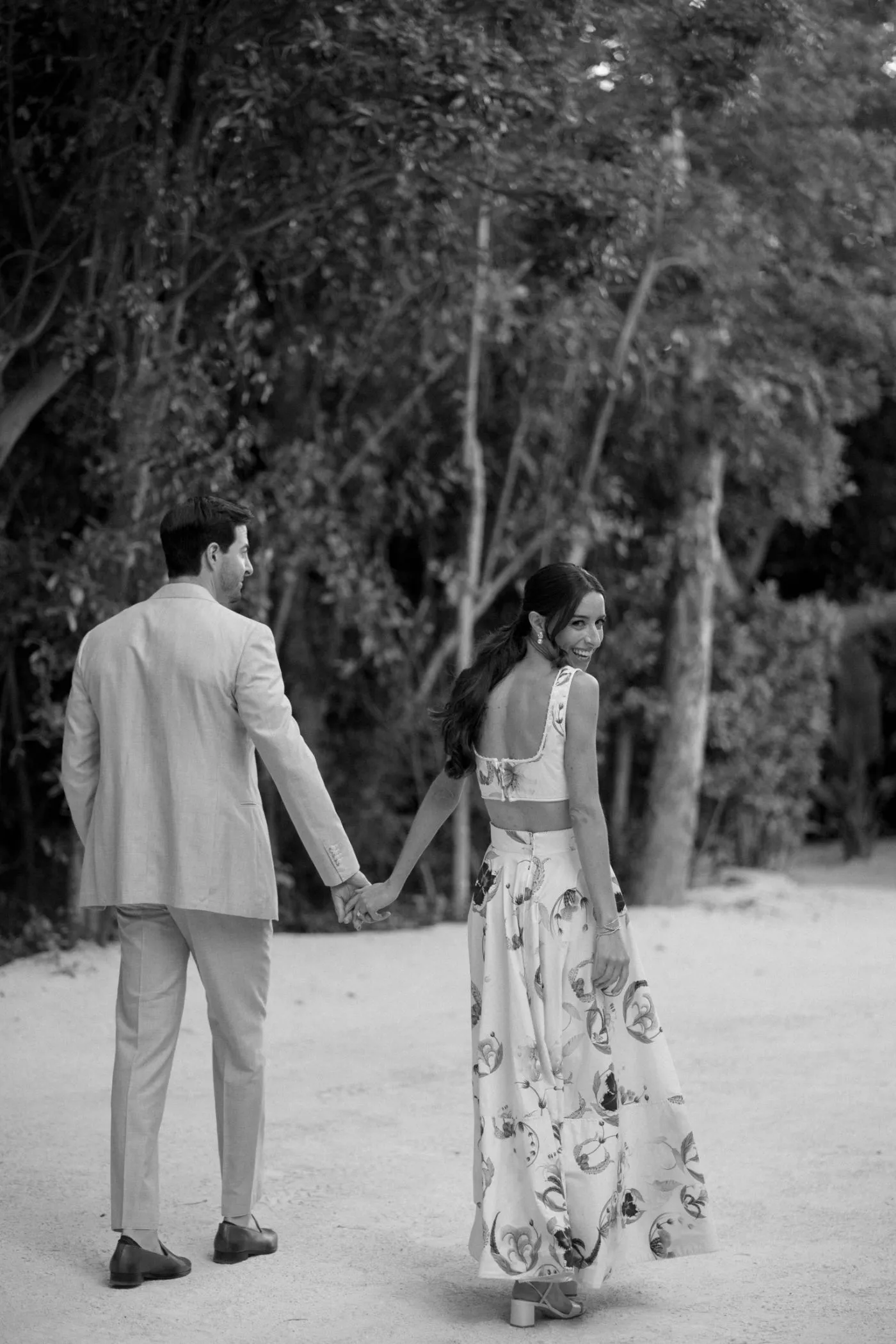 Couple walking a sandy path hand in hand, the bride glancing back and laughing