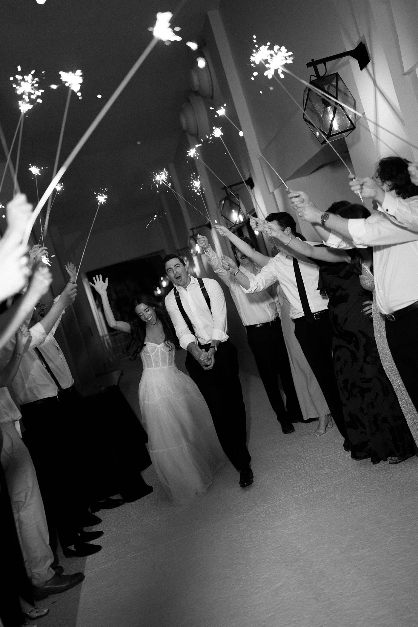 Bride and groom walking through an arch of sparklers held by guests at night