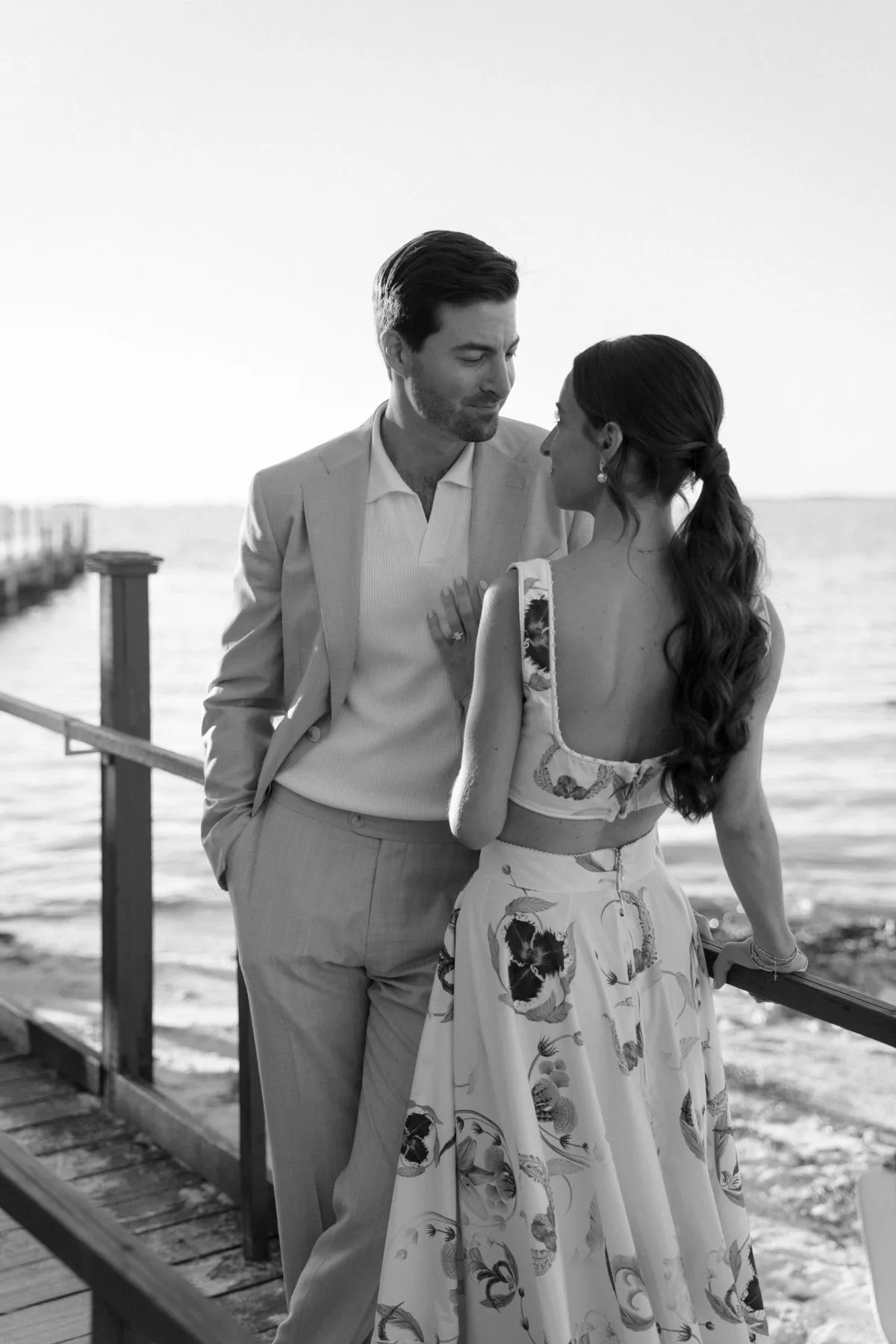 Couple leaning together on a wooden dock railing above the water at dusk