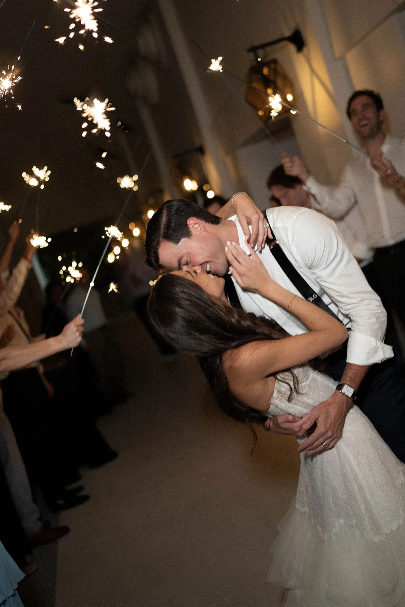 Groom dipping the bride for a kiss as guests hold sparklers overhead
