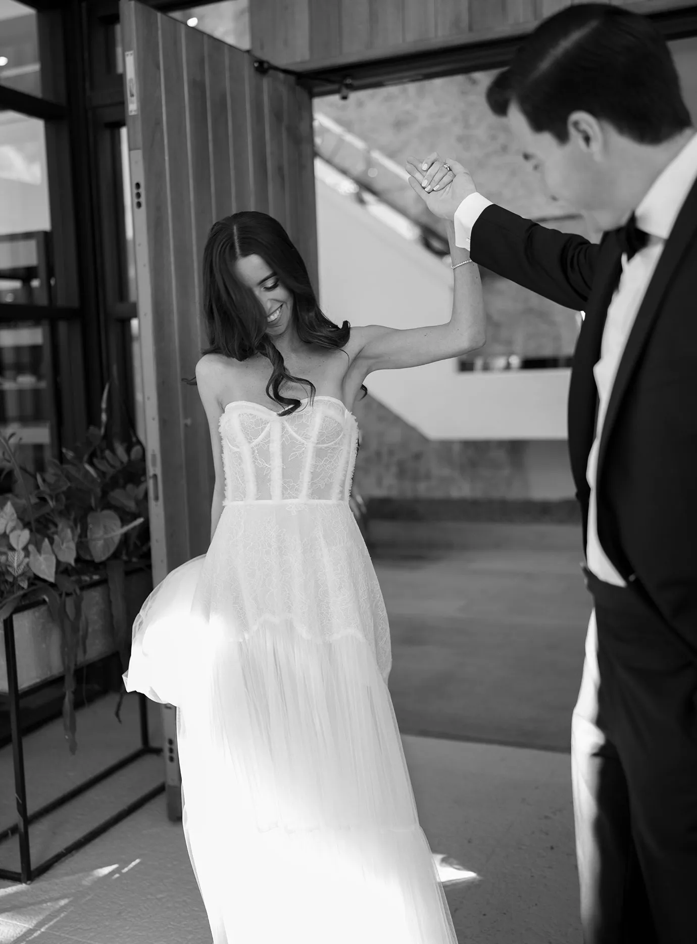 Groom in a tuxedo spinning the bride under his arm in a doorway