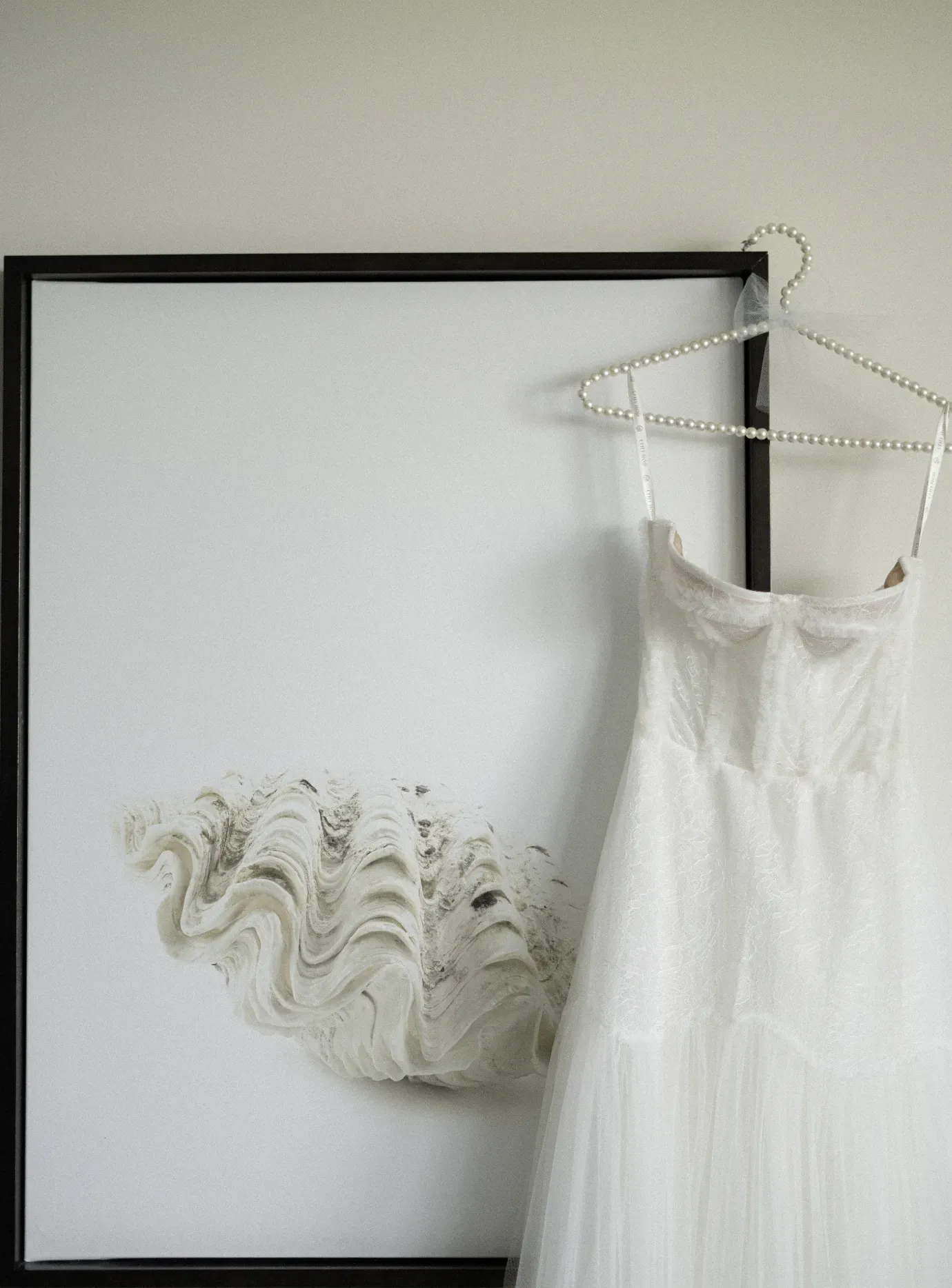 Lace wedding dress on a pearl hanger beside a framed print of a clam shell