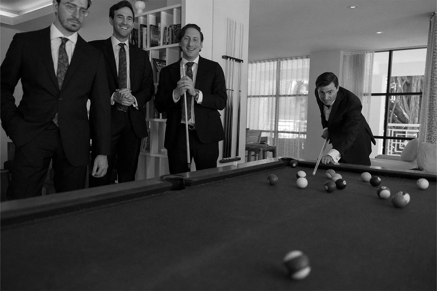Four men in suits playing pool, one leaning in to take a shot