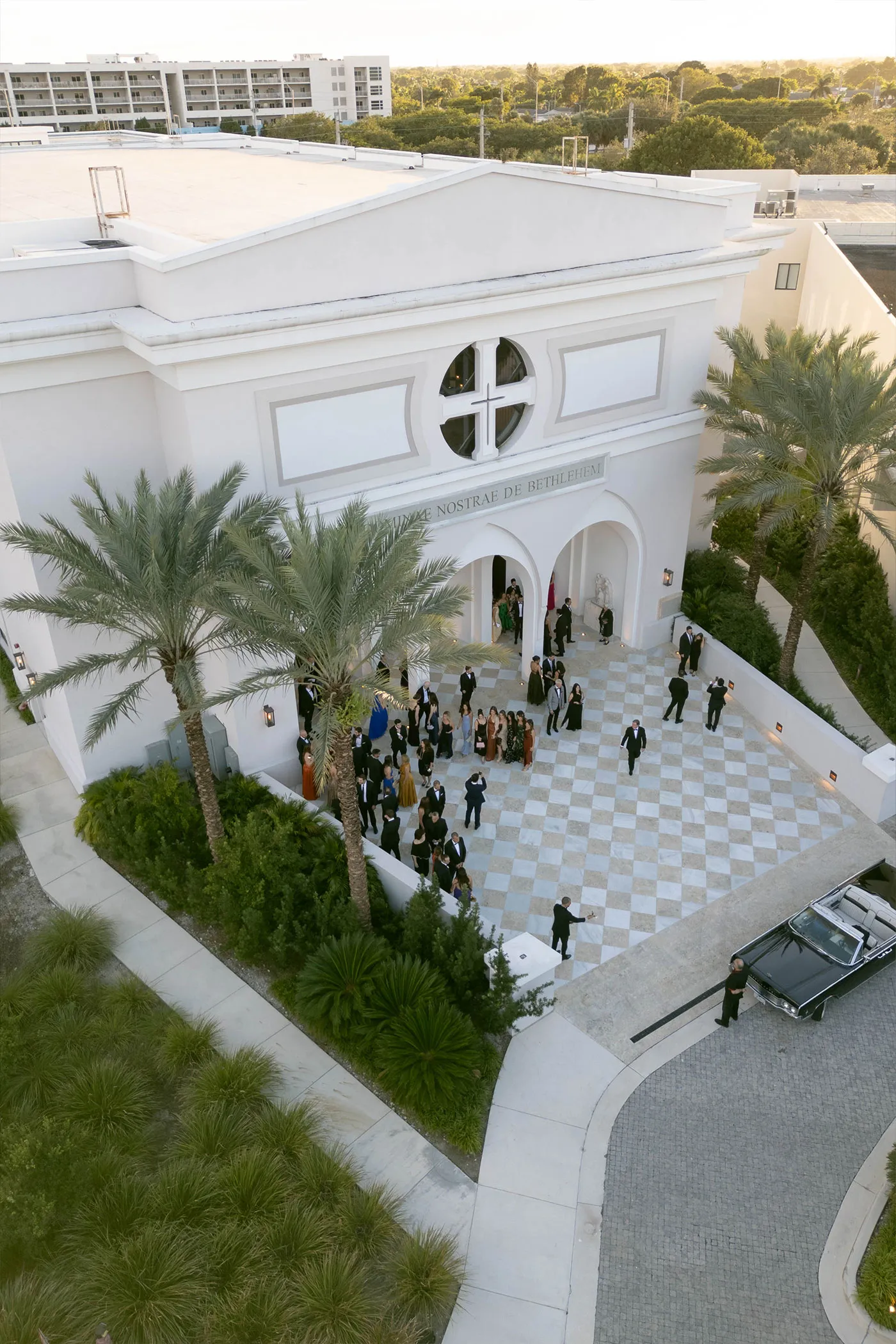 Aerial view of guests in black tie on a checkered church forecourt lined with palms
