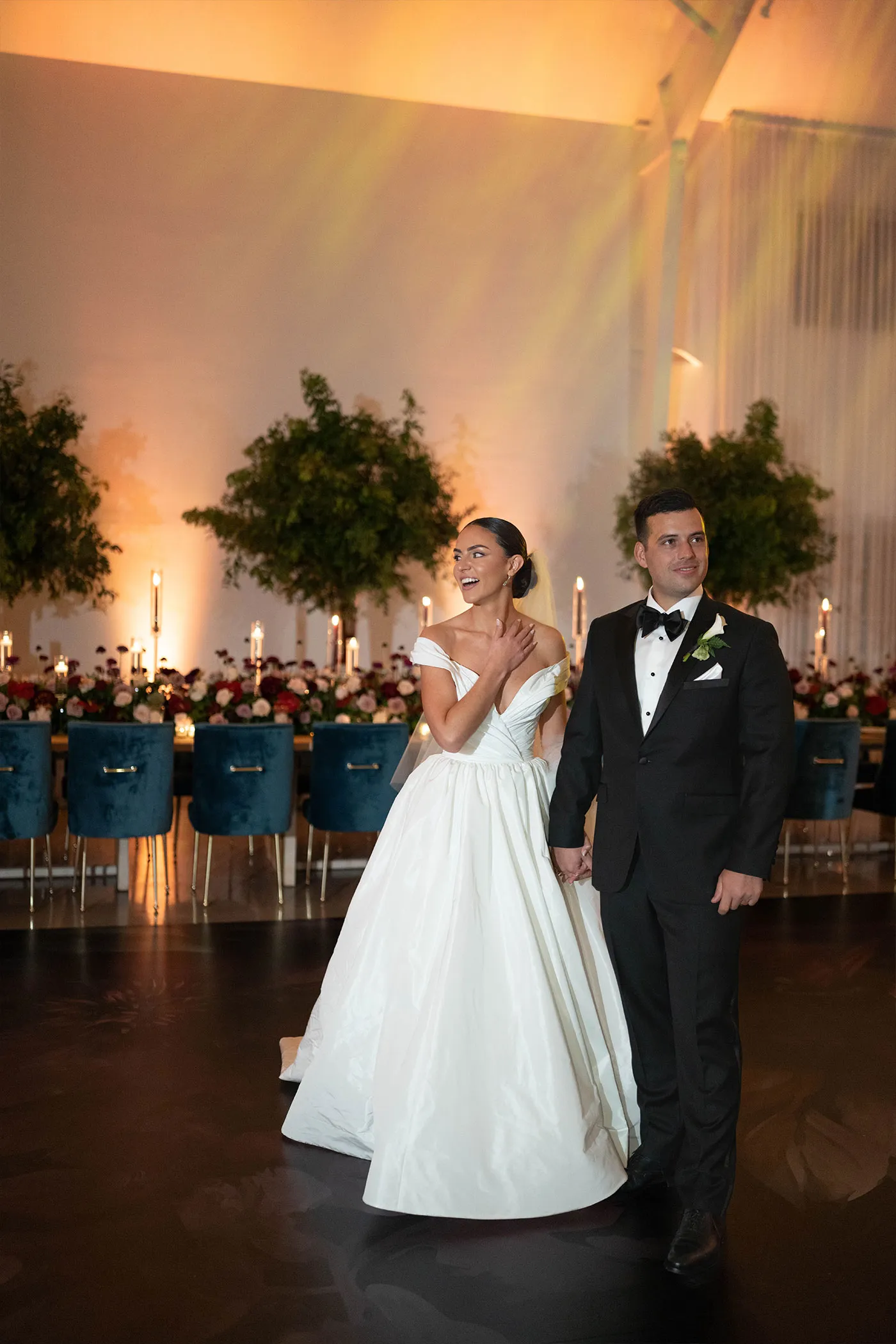 Bride in a full ballgown and groom in a tuxedo entering a candlelit reception