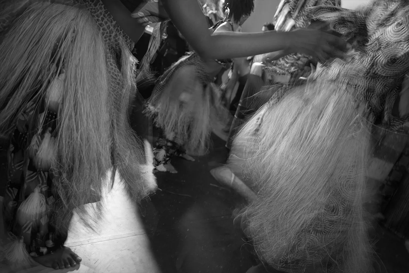 Dancers in raffia skirts moving barefoot in a blurred black and white frame