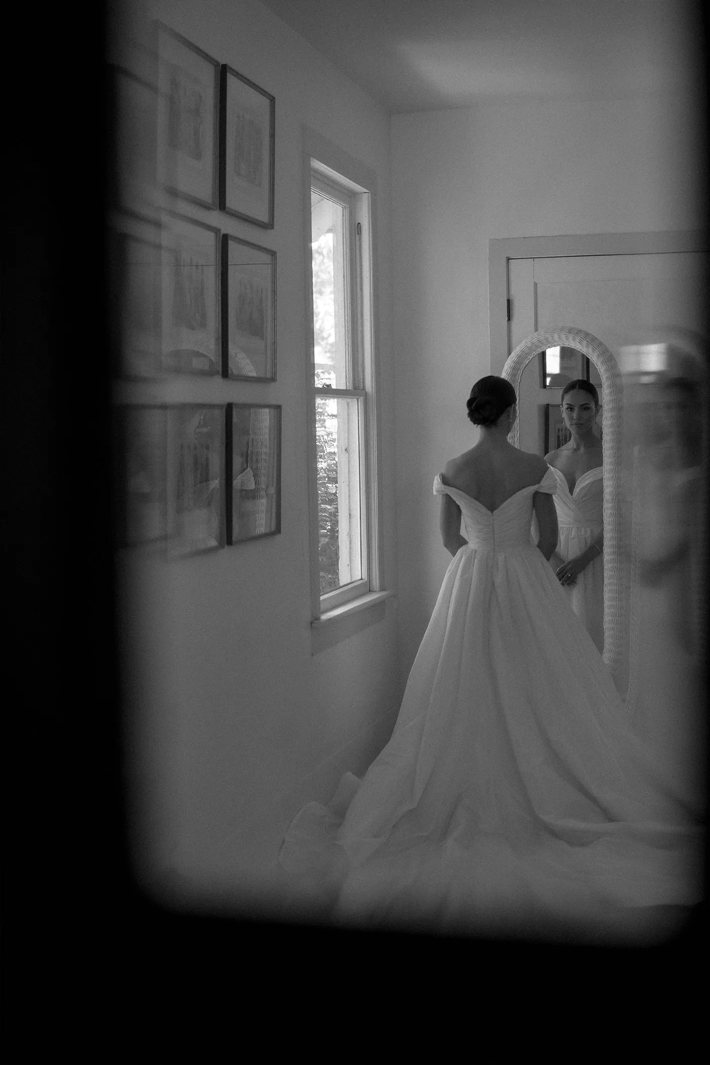 Bride in a ball gown facing an arched mirror, seen through a doorway