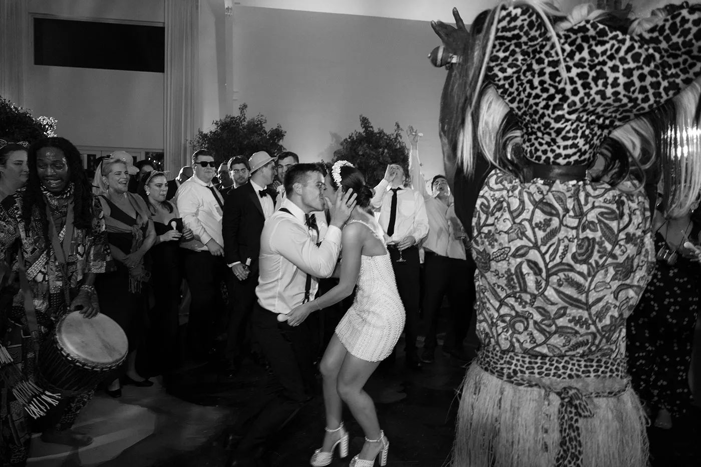 Bride in a short beaded dress kissing the groom on the dance floor beside a drummer