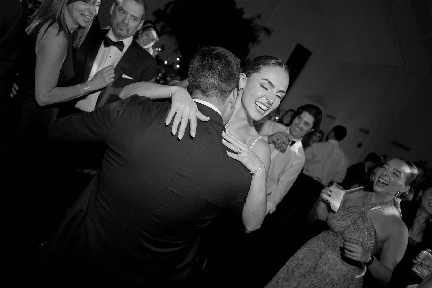 Bride laughing with her arms around the groom on a crowded dance floor