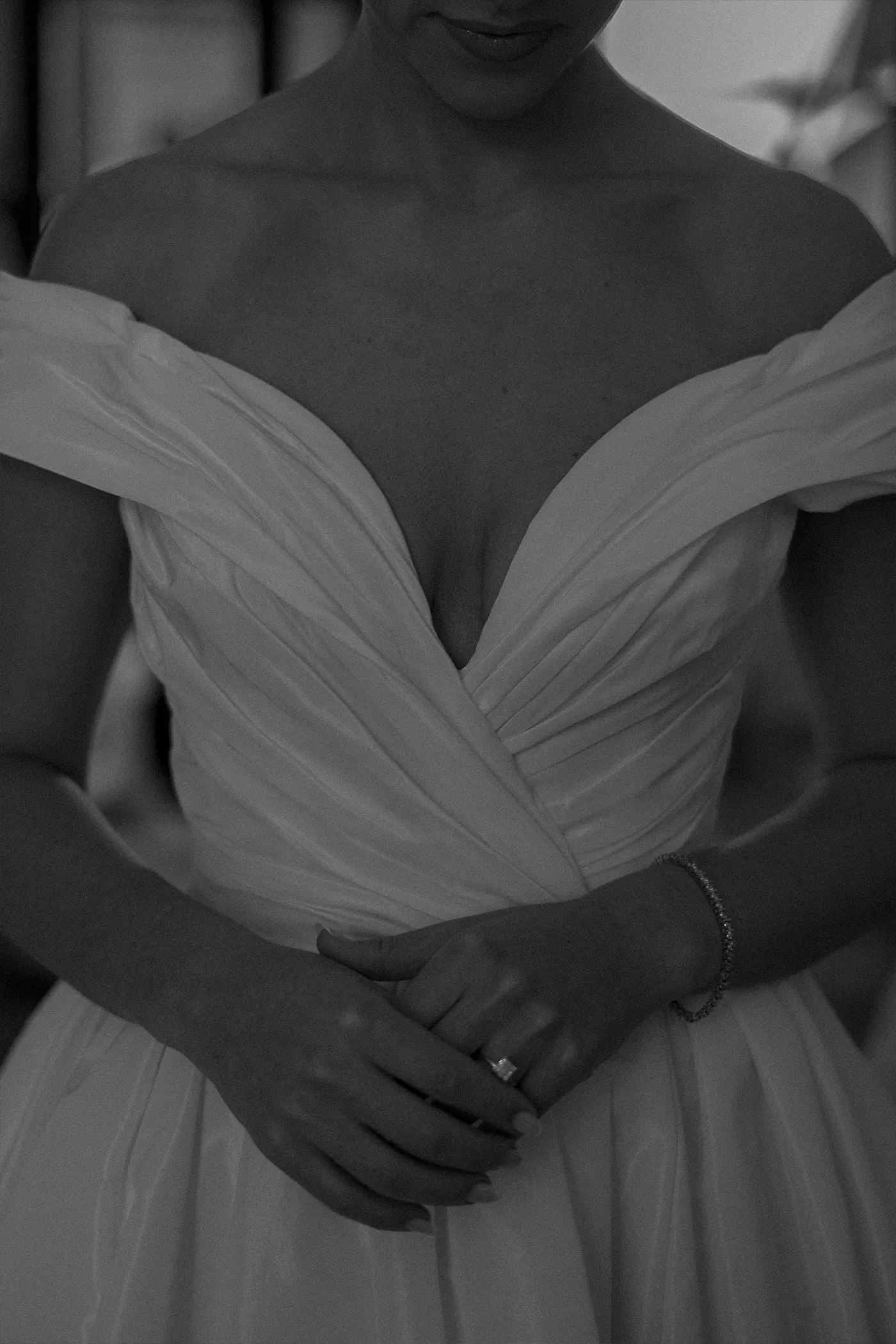 Close crop of a bride's hands clasped over the pleated bodice of her gown