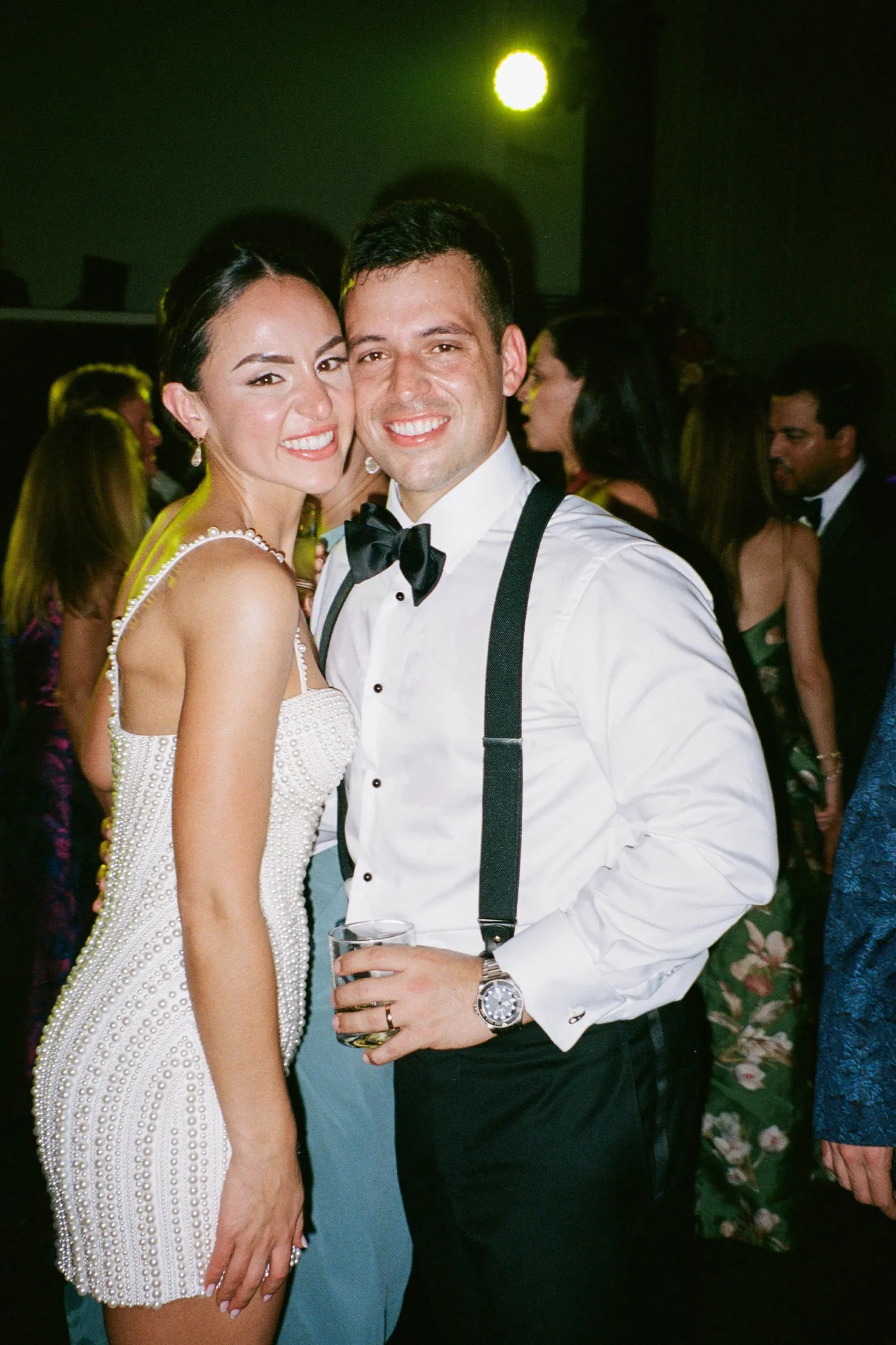 Bride in a pearl-beaded mini dress cheek to cheek with the groom at the party