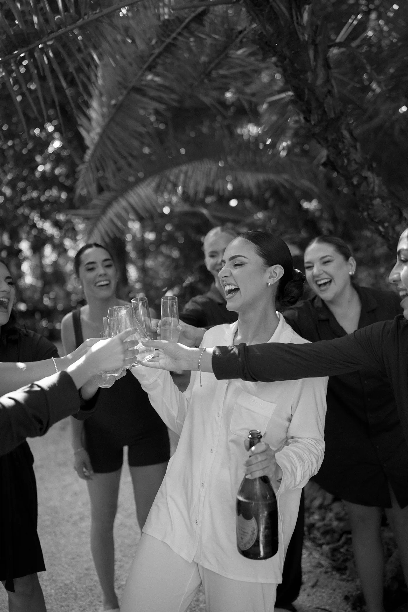 Bride in white pyjamas holding a champagne bottle and toasting with her bridesmaids