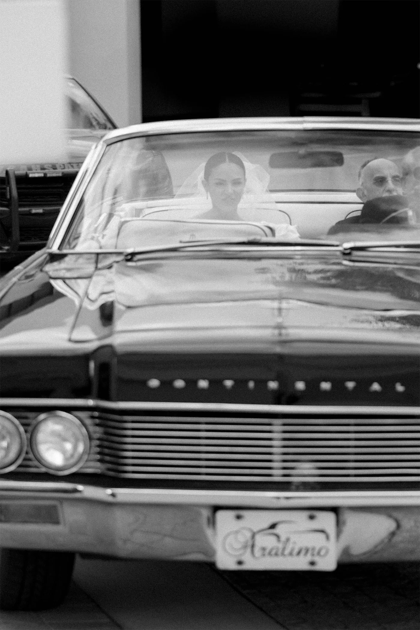 Bride in a veil seen through the windshield of a vintage convertible, black and white