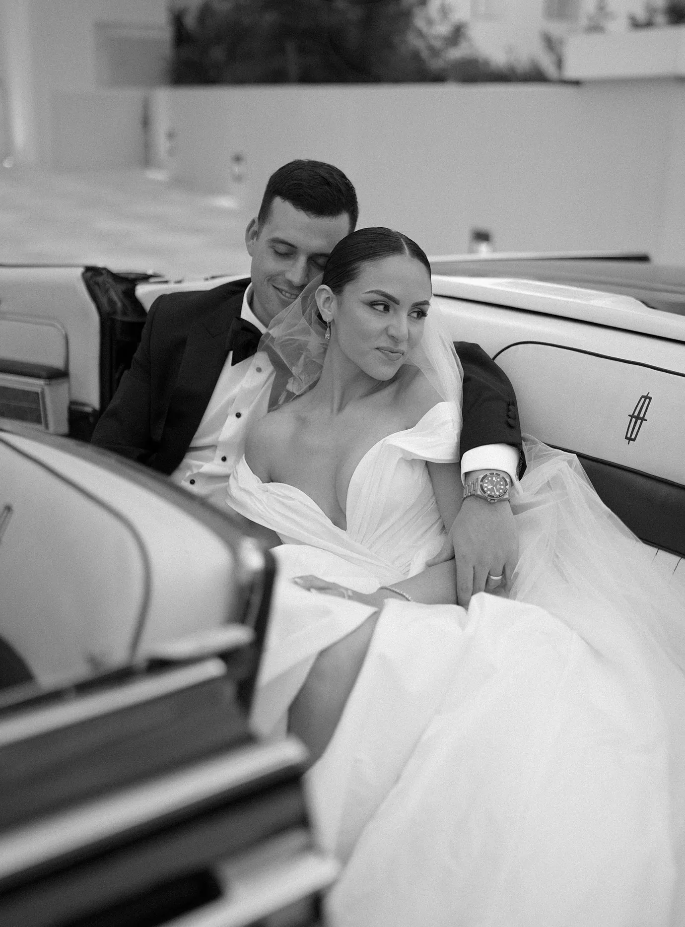 Bride and groom sitting close in the back seat of a vintage convertible