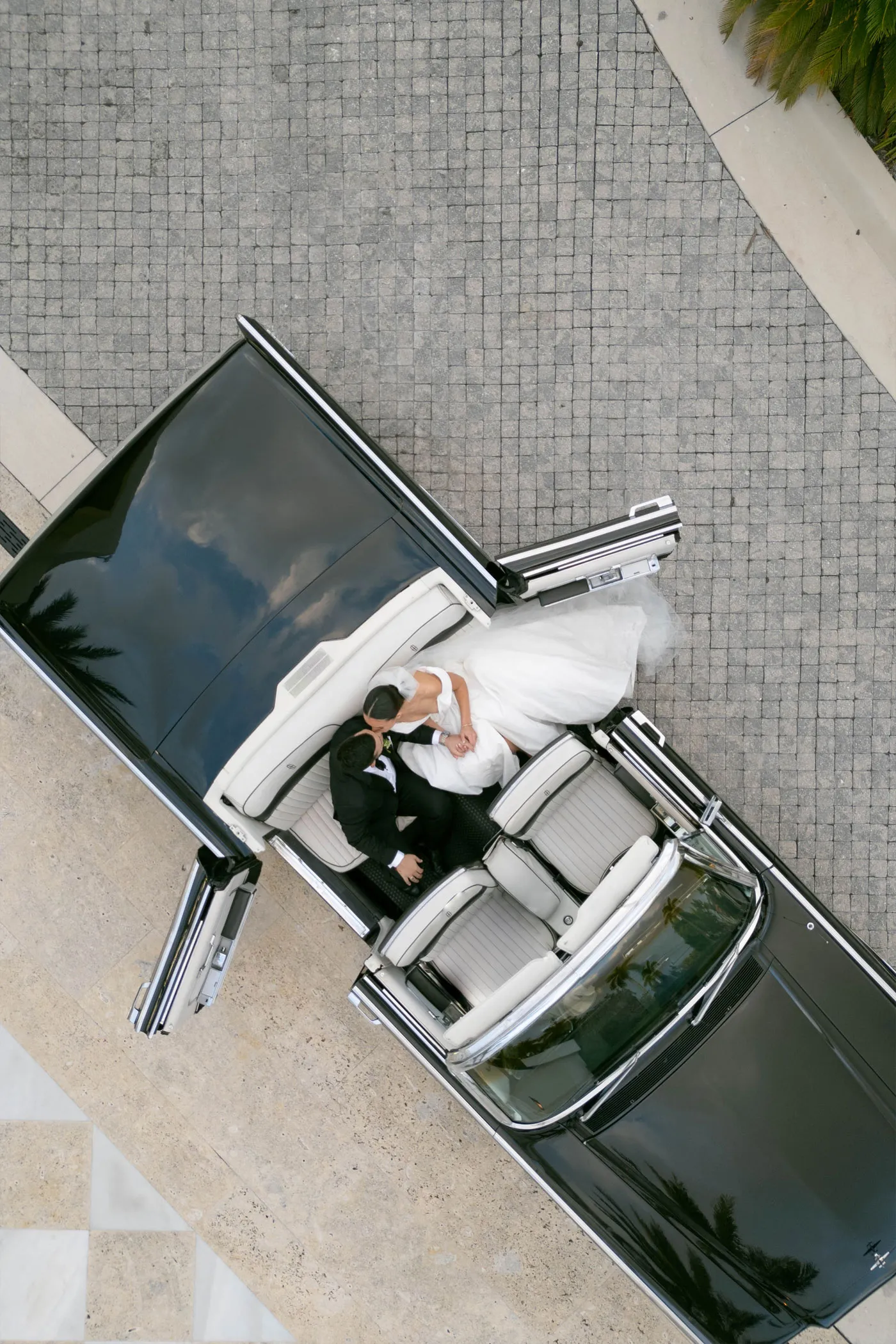Overhead view of a couple seated in a black convertible on a cobblestone drive