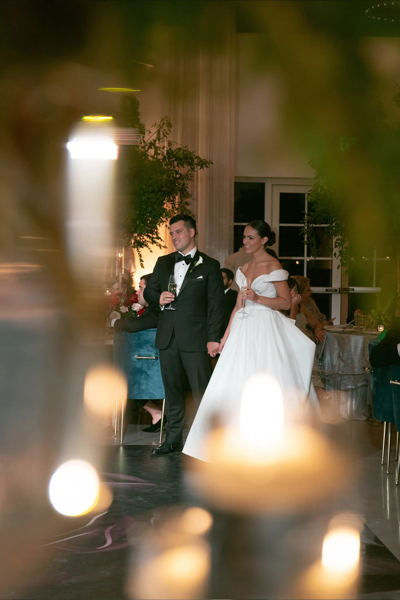 Bride and groom holding champagne as they enter a candlelit reception